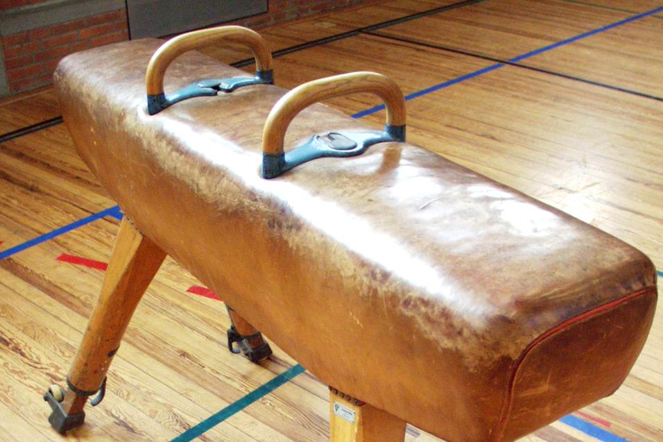 Turnbank mit Holzgriffen auf einem Holzfußboden in einer Sporthalle.